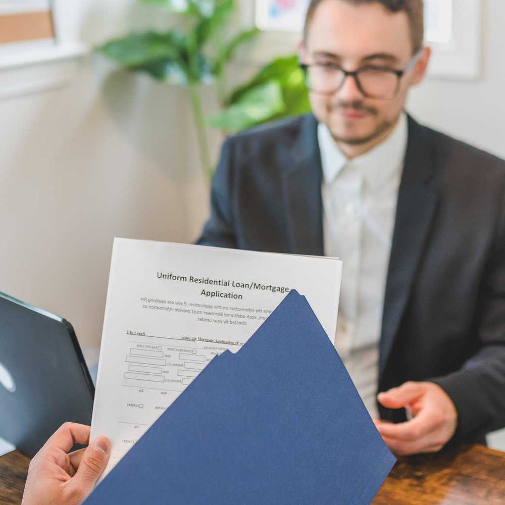 Person holding folder of application to hand to man sitting